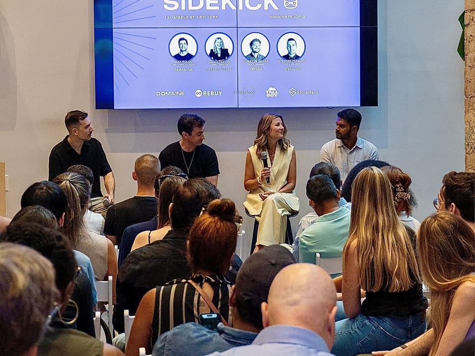 Three panelists on stage at Shopify New York, with Meet Your Sidekick on the screen behind them.