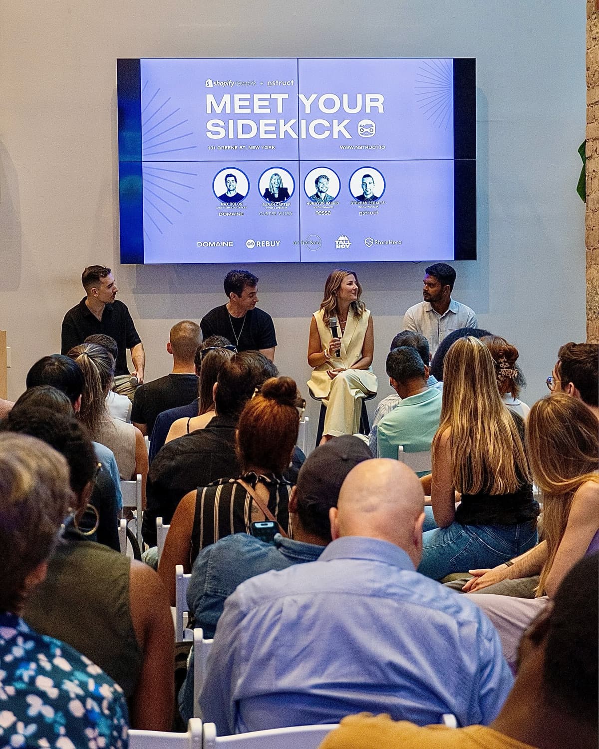 Three panelists seated on stage at Shopify New York. The screen behind them reads Meet Your Sidekick, with Shopify and Nstruct logos below.