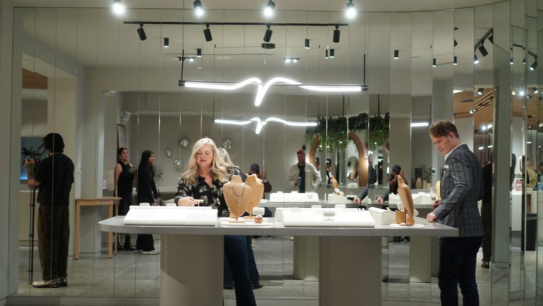 Two people in conversation beside a jewellery display and a vase of flowers.