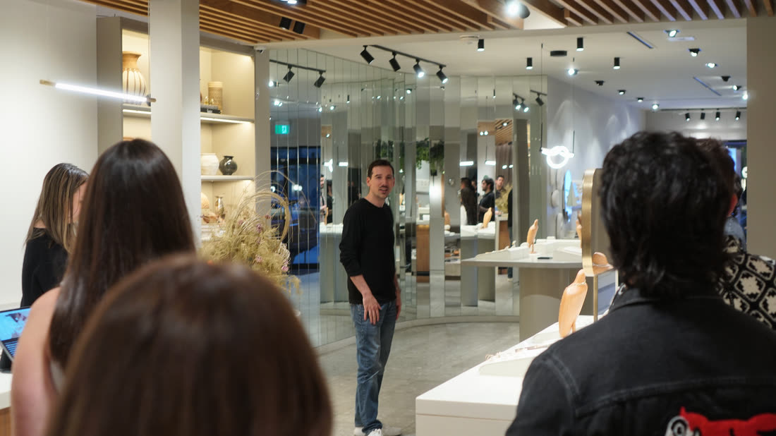 People at a counter toward the back of the store, with shopping bags and display cases.